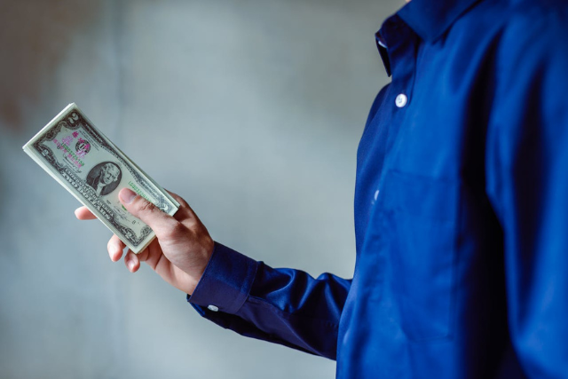 a-person-wearing-a-blue-shirt-holds-a-stack-of-u-s-dollar-bills-in-one-hand